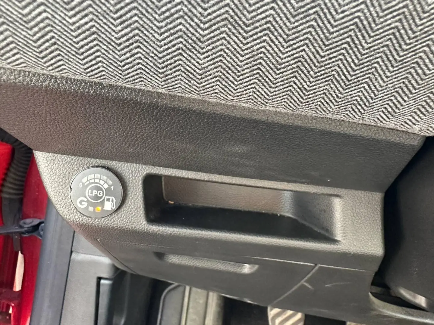 Détail intérieur montrant le témoin de carburant GPL sous le siège avant d’une Renault Clio Rouge Flamme.