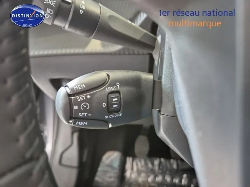 Gros plan sur la commande de régulateur de vitesse à gauche du volant dans une Peugeot 208 gris Artense 2025.