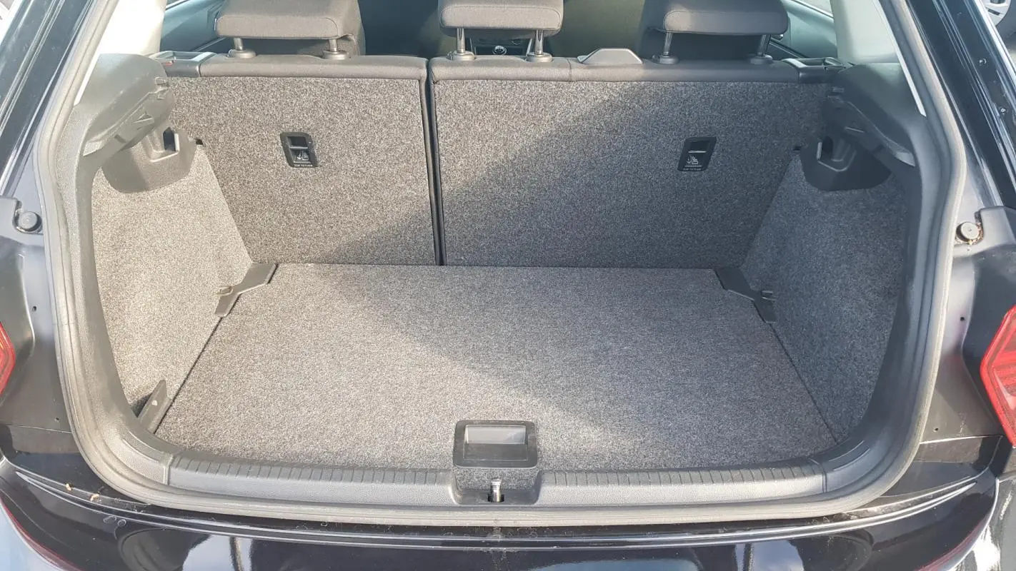 Coffre ouvert d'une Volkswagen Polo noire de 2018, vue arrière montrant l'espace de chargement vide et tapis gris.