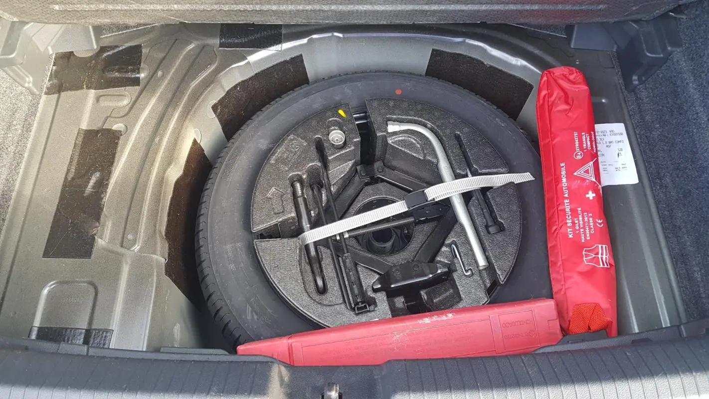 Gros plan sur la roue de secours et le kit de sécurité rouge dans le coffre d'une Volkswagen Polo noire de 2018.