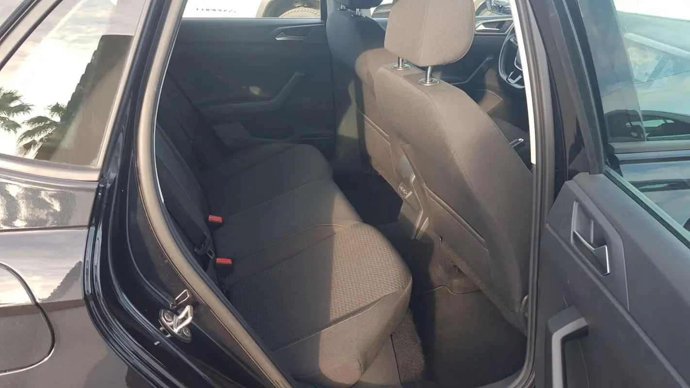 Vue intérieure côté arrière gauche d'une Volkswagen Polo noire 2018, montrant la banquette arrière et les sièges avant en tissu noir.