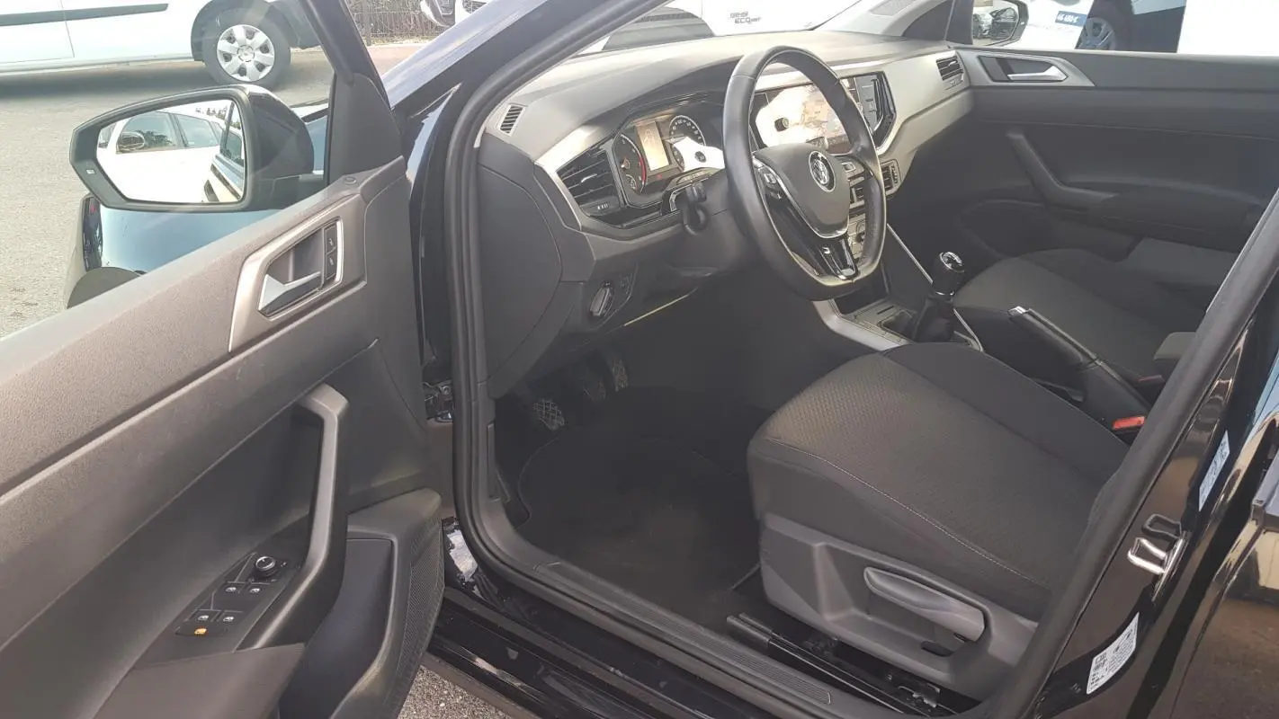 Intérieur côté conducteur d'une Volkswagen Polo noire 2018, volant multifonctions et siège réglable en hauteur visibles.