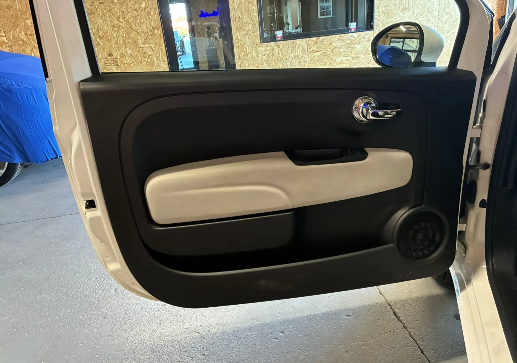 Vue intérieure de la porte avant gauche blanche d'une FIAT 500 2021, avec panneau noir et beige et poignée chromée.