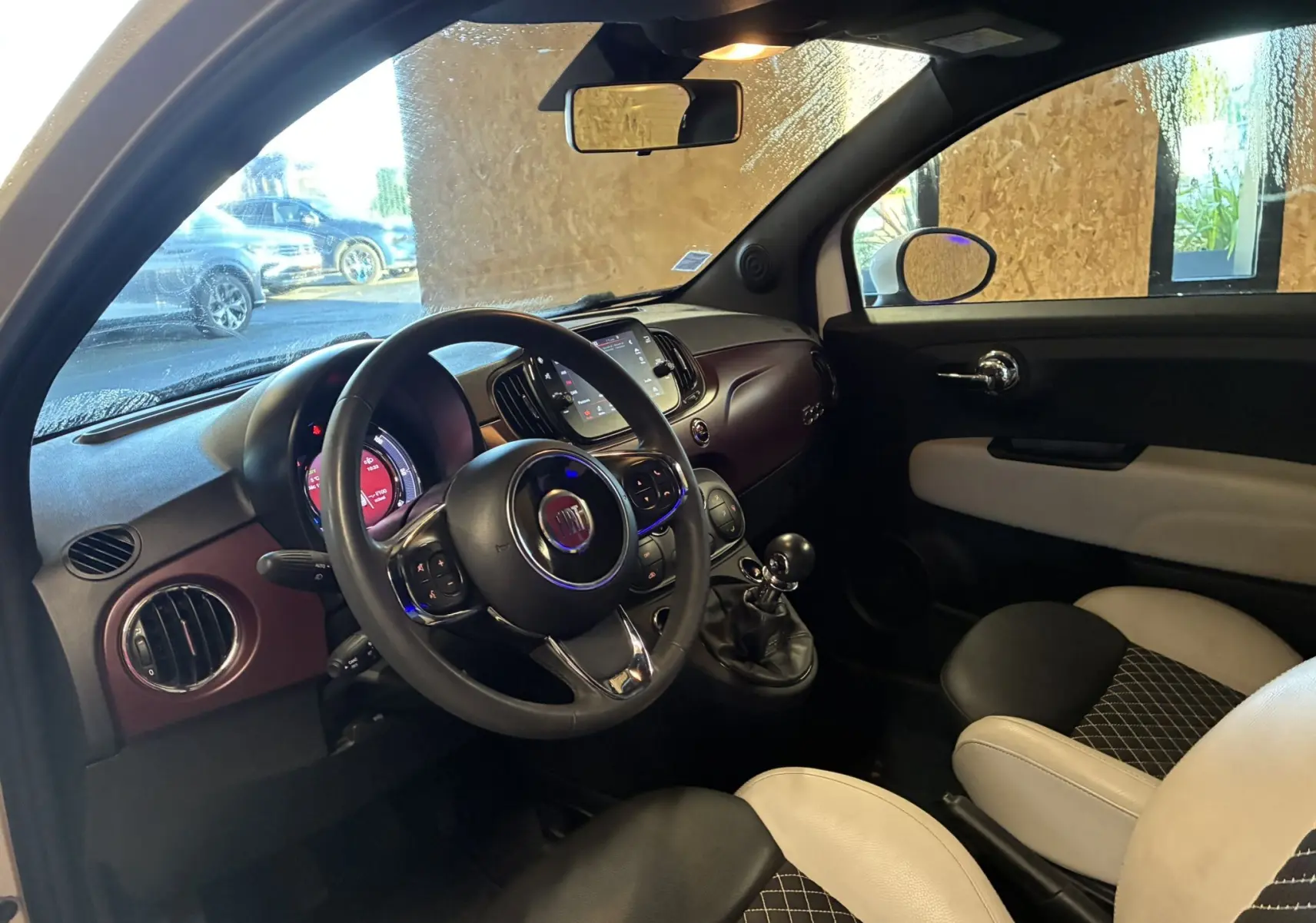 Vue intérieure côté conducteur de la Fiat 500 blanche, montrant le volant, tableau de bord et sièges bicolores noirs et blancs.