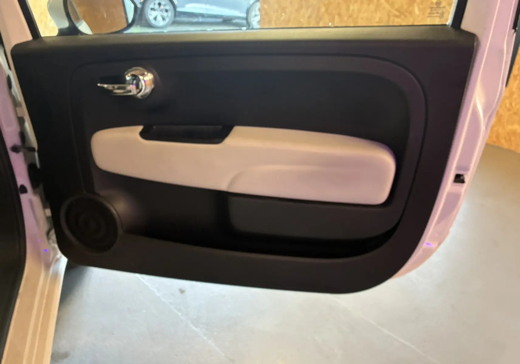 Vue intérieure de la porte côté gauche d'une Fiat 500 blanche, avec poignée chromée et panneau bicolore noir et beige.