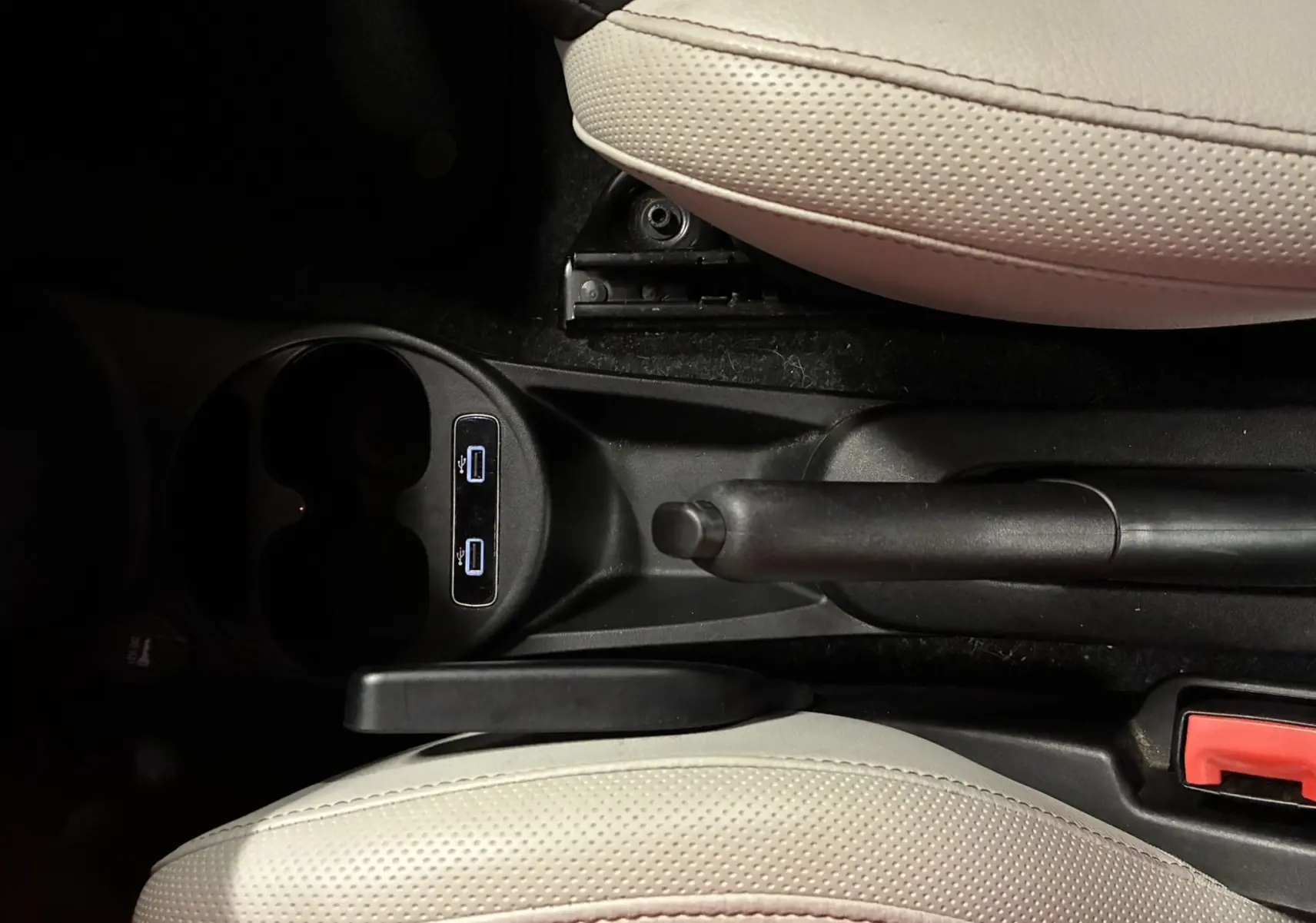 Vue plongeante sur la console centrale de la Fiat 500 blanche, avec frein à main, porte-gobelets et sièges en tissu clair.