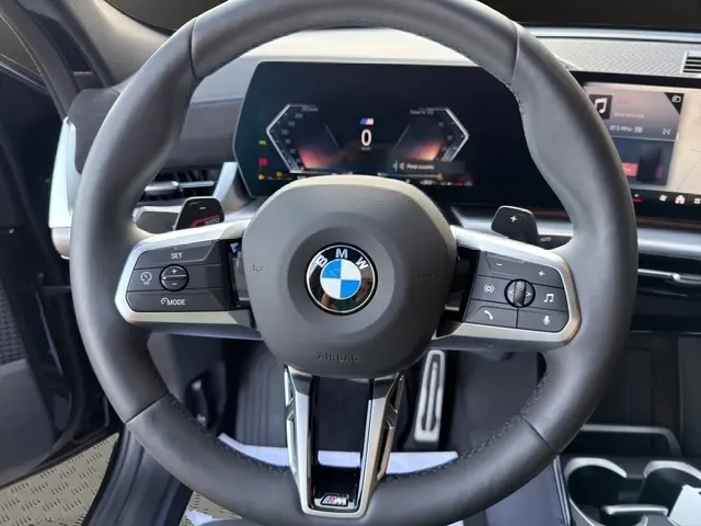 Vue rapprochée du volant en cuir et alu noir du BMW X2 sDrive20d M Sport 2025 avec tableau de bord numérique en arrière-plan.