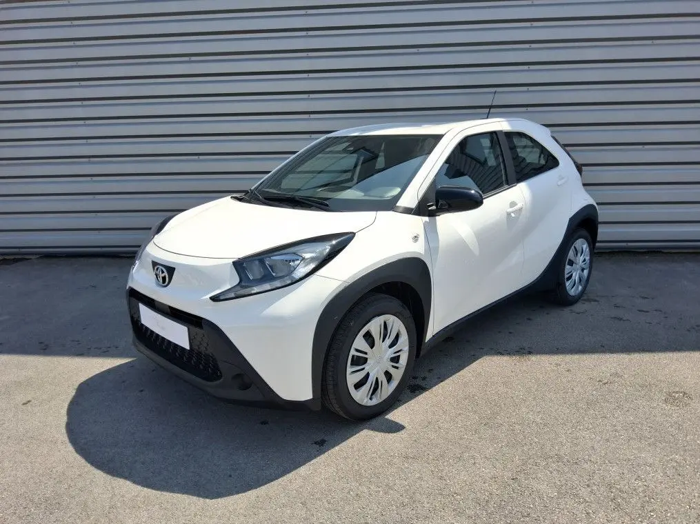 Toyota Aygo X blanc pur vue 3/4 avant droit, avec protections noires autour des roues et rétroviseurs noirs.