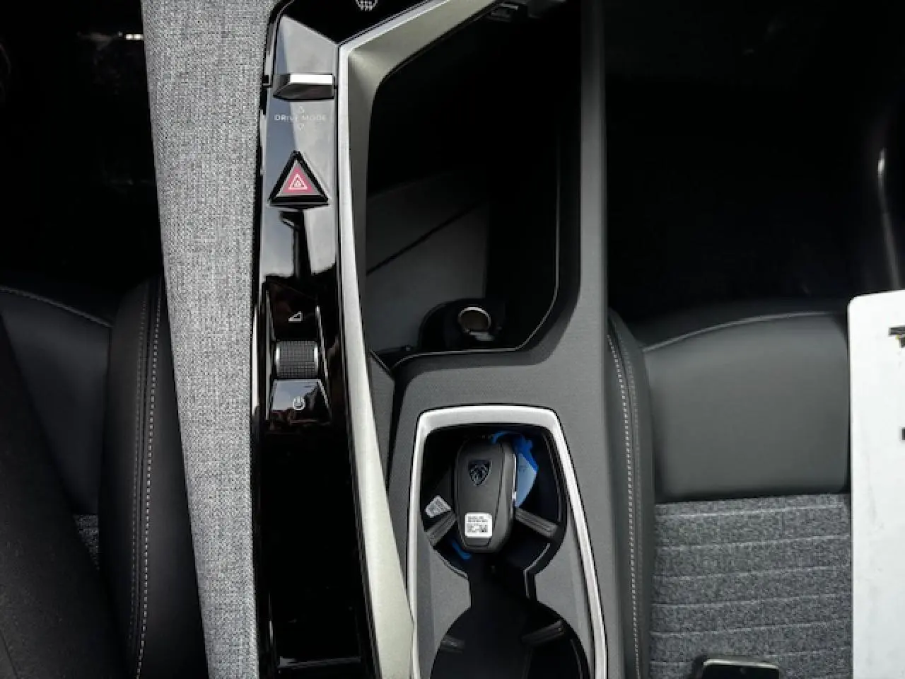 Gros plan sur la console centrale du Peugeot 5008 III avec clé, finition tissu gris et cuir noir.