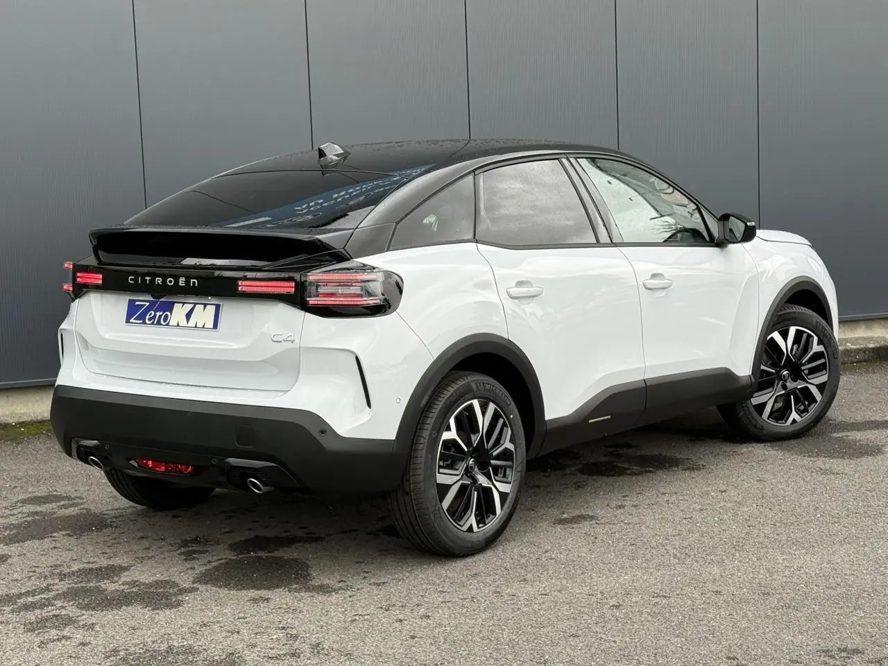 Vue 3/4 arrière droite d'une Citroën C4 hybride blanche Okénite avec toit noir Perla Nera et jantes alliage 18 pouces.