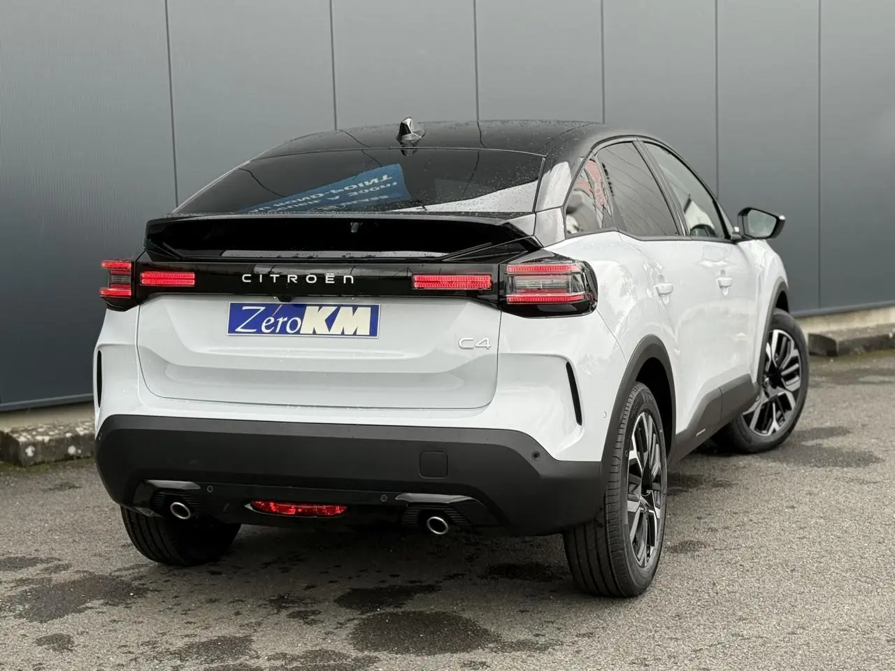 Vue 3/4 arrière droite d'une Citroën C4 blanche Okénite avec toit noir Perla Nera et feux arrière LED allumés.
