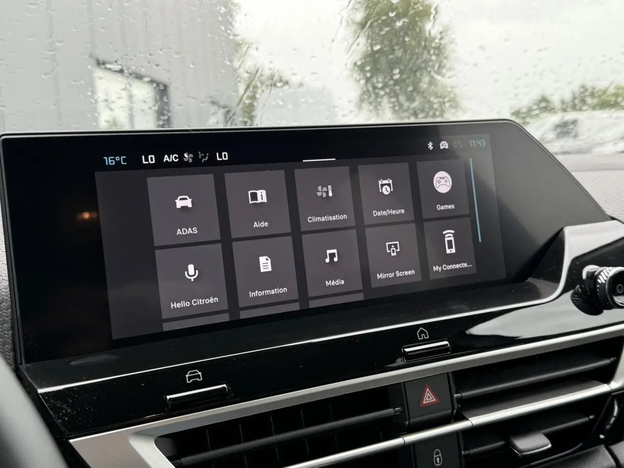 Écran tactile central du tableau de bord du Citroën C4 blanc, affichant le menu principal sous la pluie.