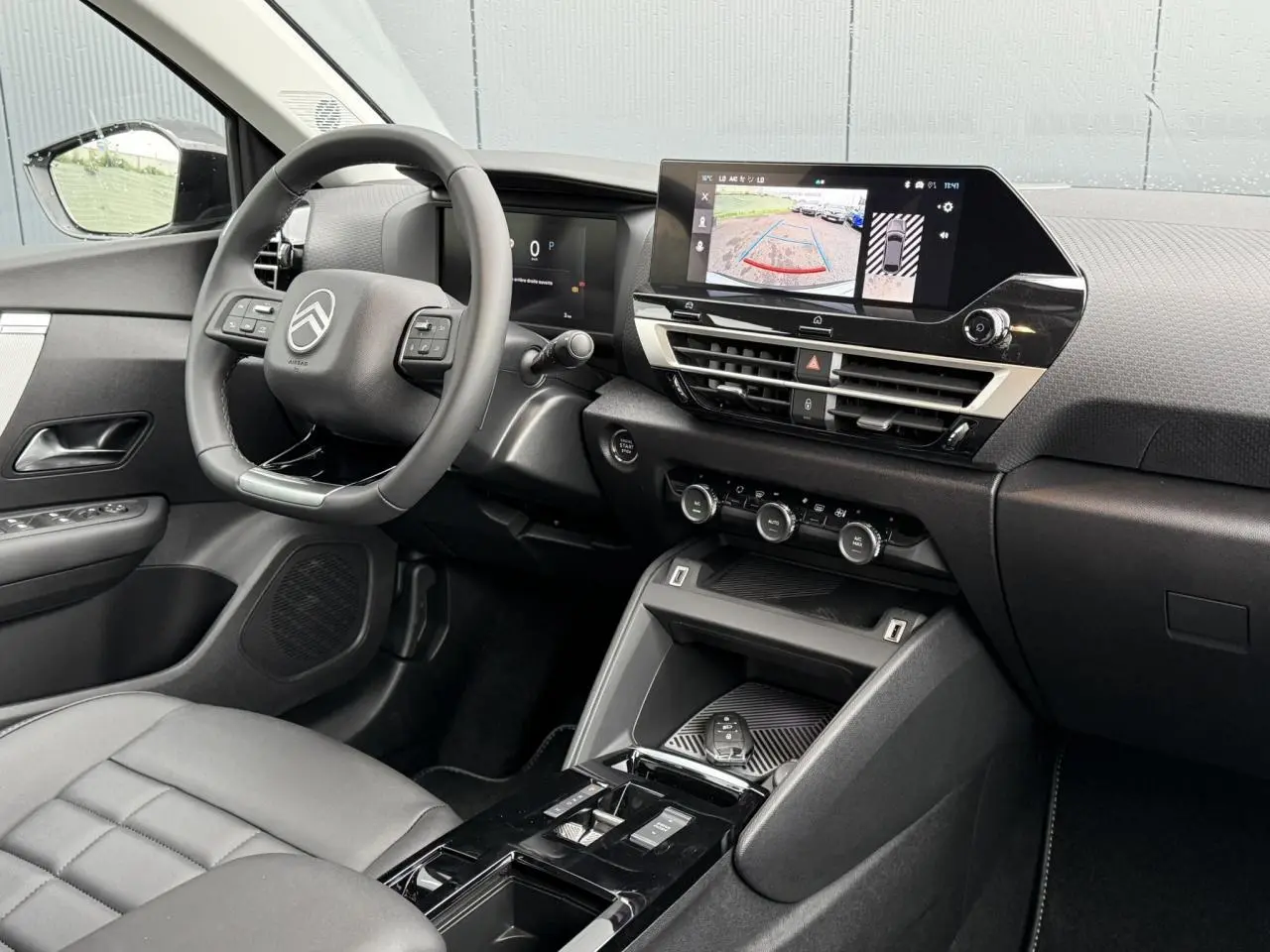 Vue intérieure côté conducteur de la Citroën C4 hybride 2025 avec tableau de bord noir et écran tactile affichant la caméra de recul.