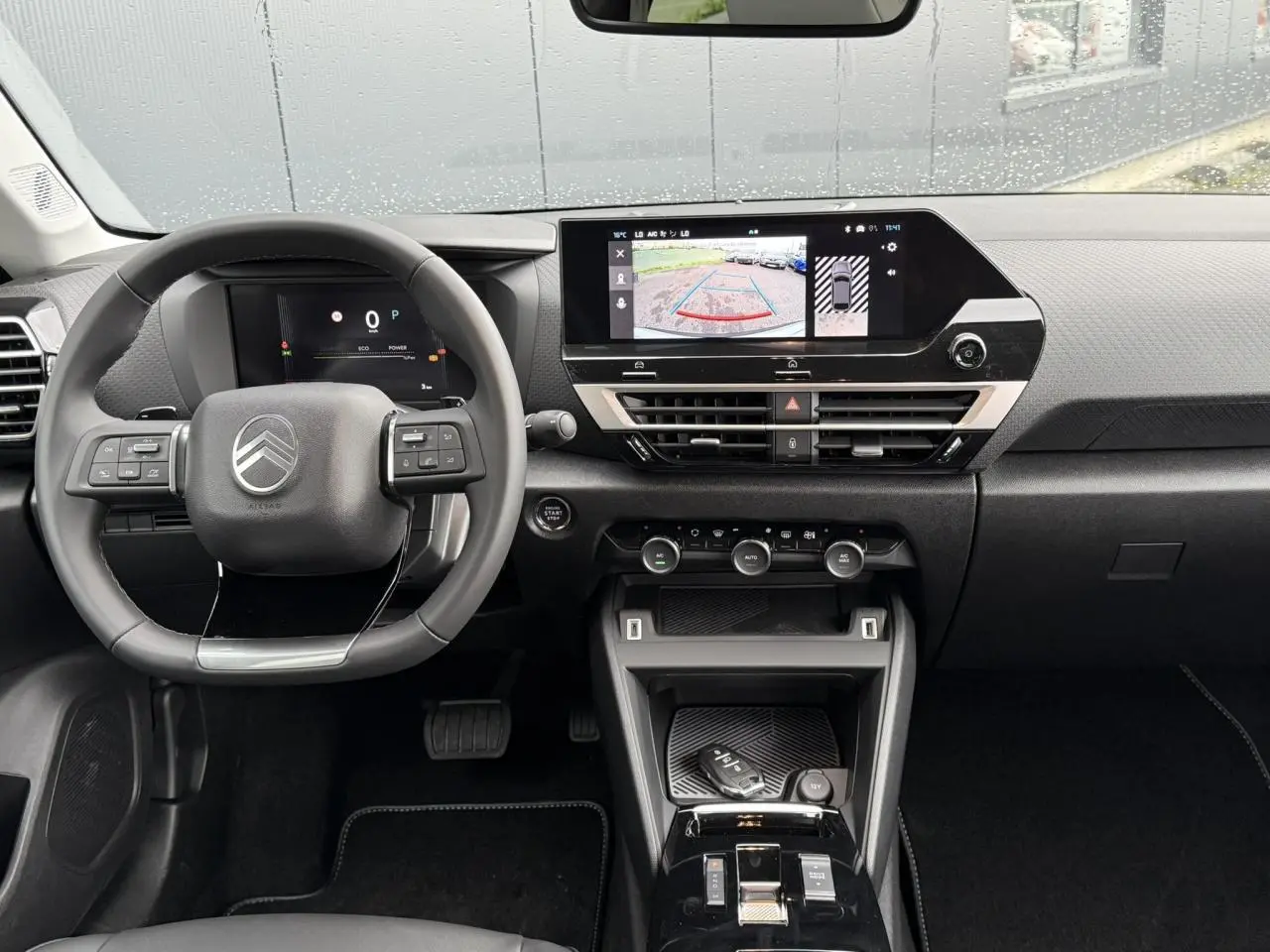 Vue frontale de l'habitacle noir du Citroën C4 2025, avec volant multifonction et écran tactile affichant la caméra de recul.