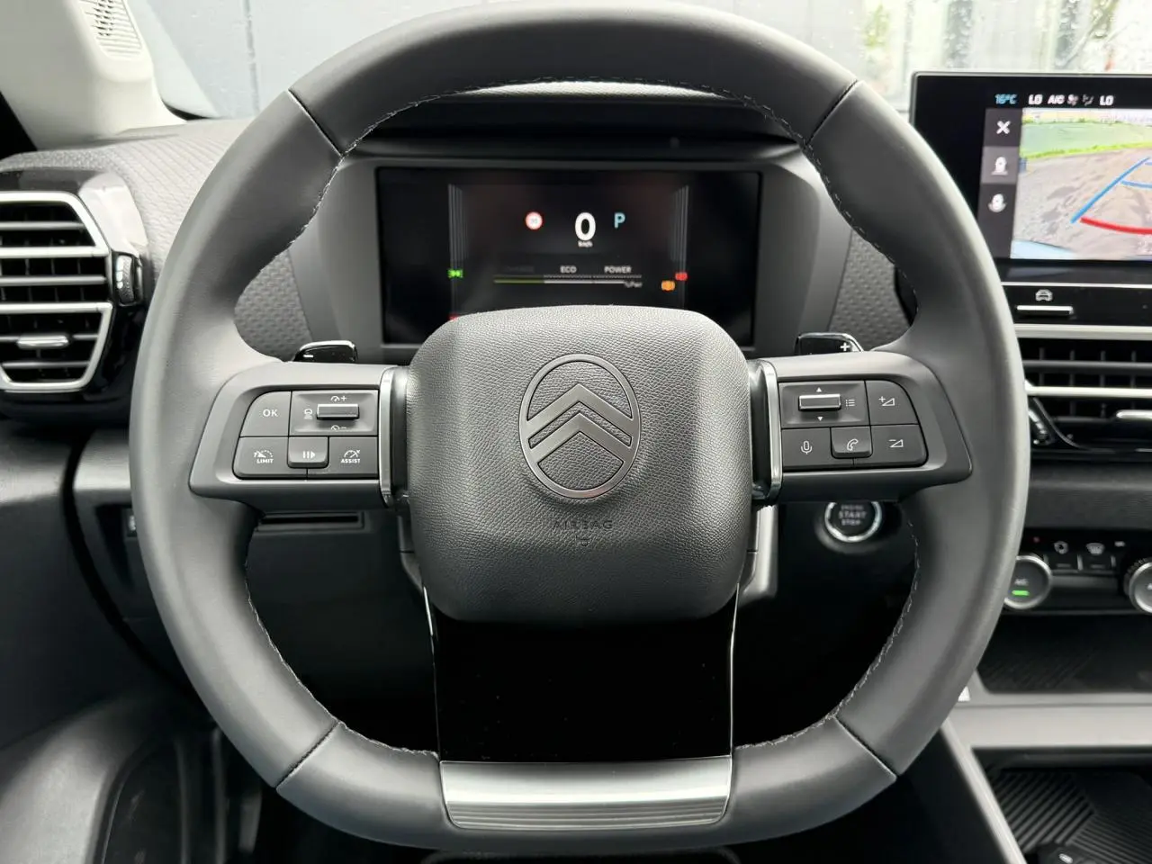 Vue frontale du volant cuir noir de la Citroën C4 2025 avec commandes intégrées et écran numérique en arrière-plan.