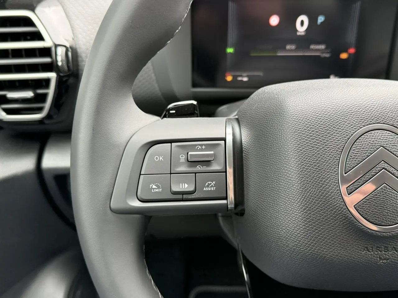 Gros plan sur le volant cuir gris du Citroën C4 2025 avec commandes intégrées et logo chromé au centre.