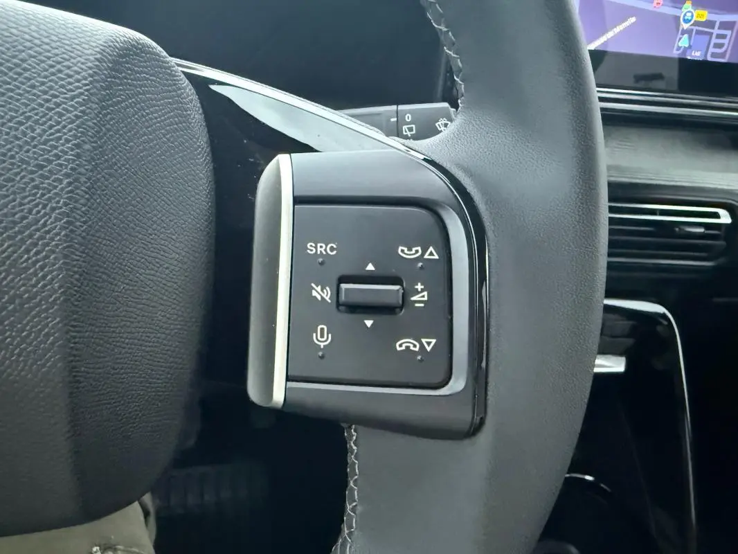 Gros plan sur les commandes multifonctions du volant noir d'une Citroën C3 gris 2025, avec écran tactile en arrière-plan.