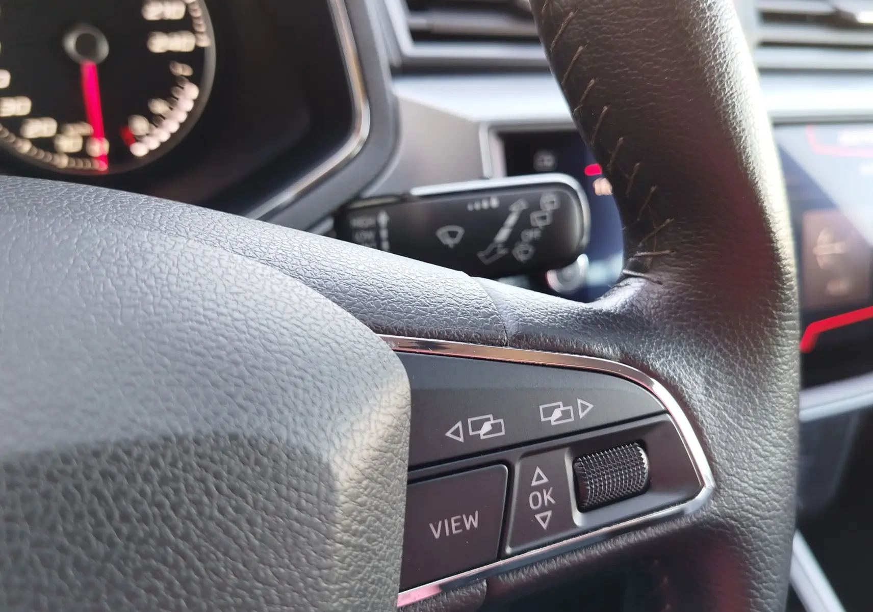 Gros plan sur les commandes multifonctions du volant en cuir noir du SEAT Arona bleu électrique, tableau de bord en arrière-plan.