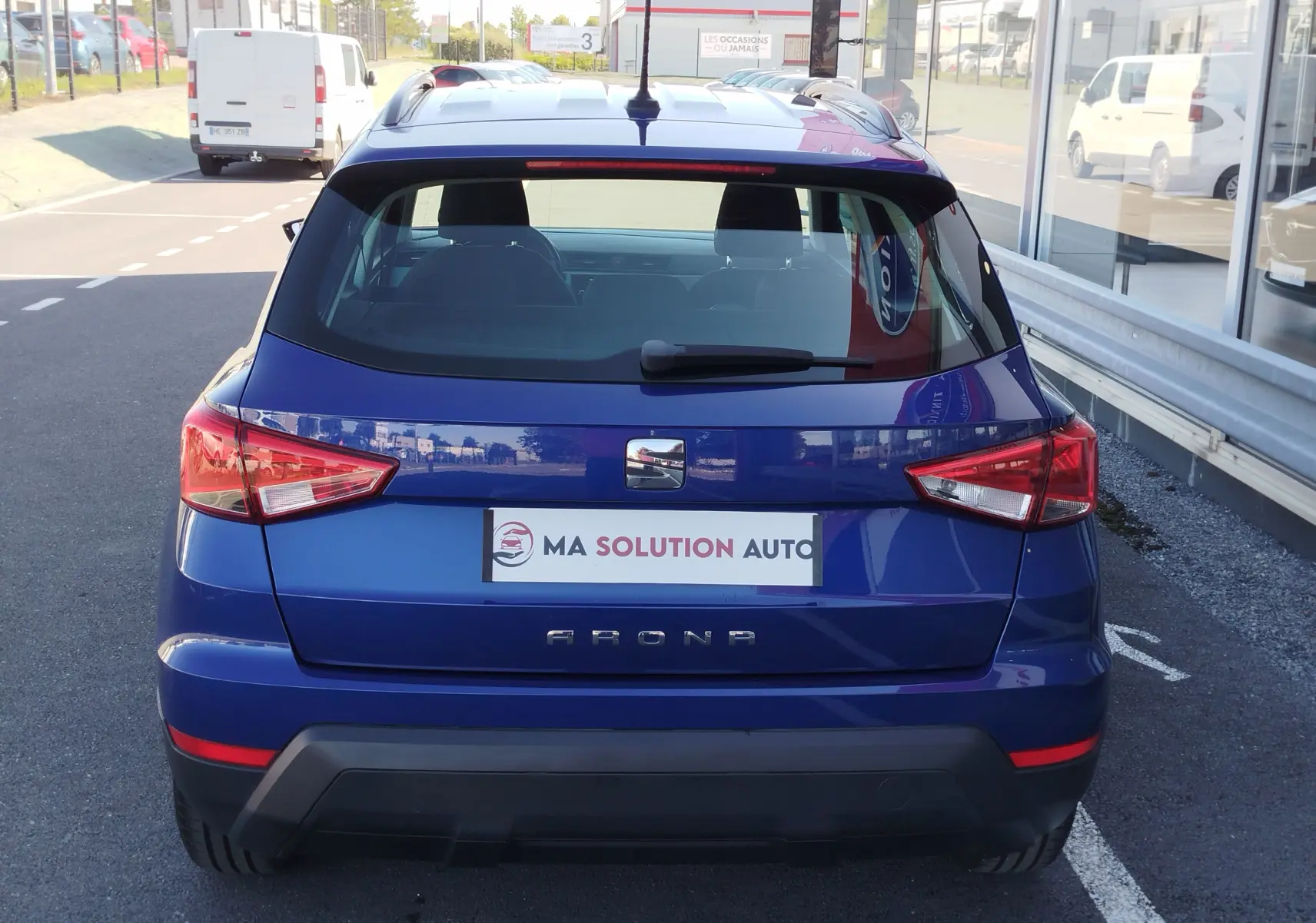 Vue arrière d'un SEAT Arona bleu électrique garé, mettant en valeur ses feux arrière anguleux et son logo central.