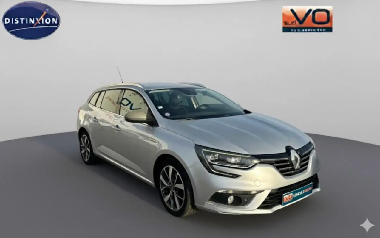 Renault Mégane Break gris clair vue 3/4 avant droit, avec jantes alliage et barres de toit visibles.