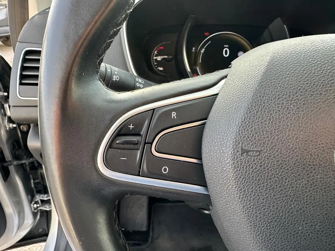 Gros plan sur le volant cuir noir de la Renault Mégane Break IV avec commandes intégrées côté gauche.