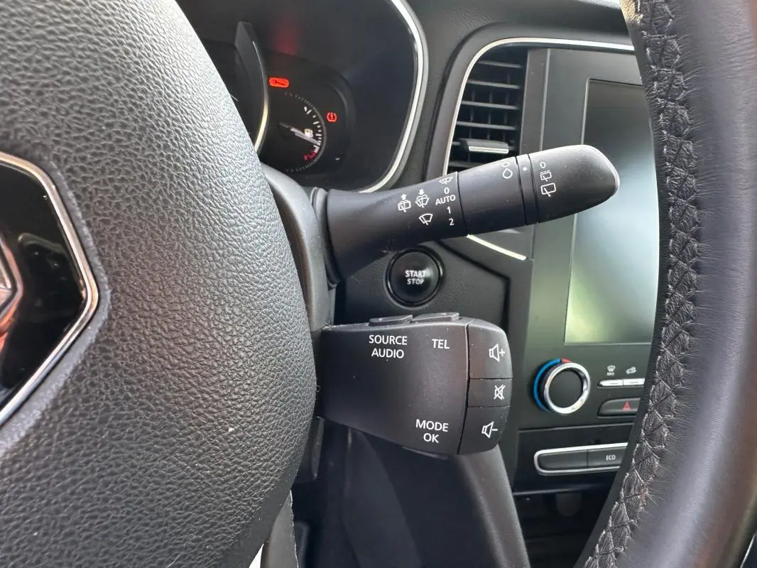 Gros plan sur le volant cuir et commandes audio d'une Renault Mégane Break gris clair, tableau de bord et écran tactile visibles.