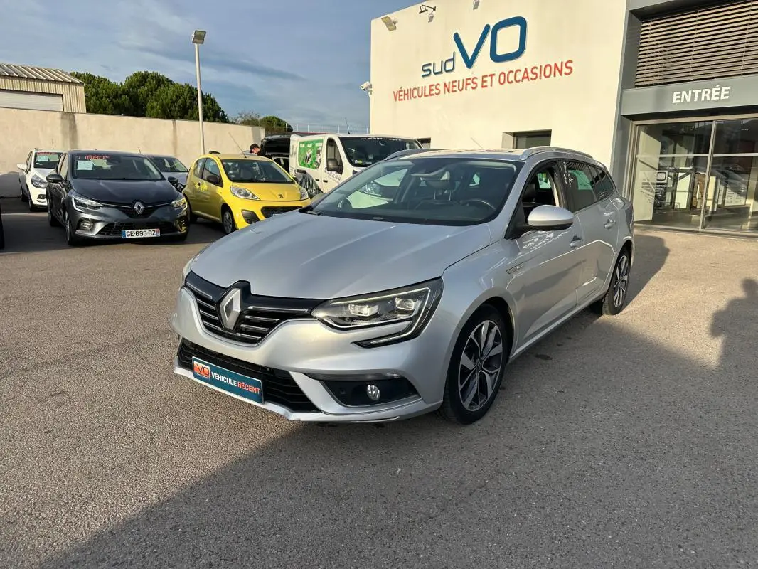 Renault Mégane Break gris clair vue 3/4 avant droit avec jantes alliage 18 pouces, barres de toit et toit ouvrant électrique.