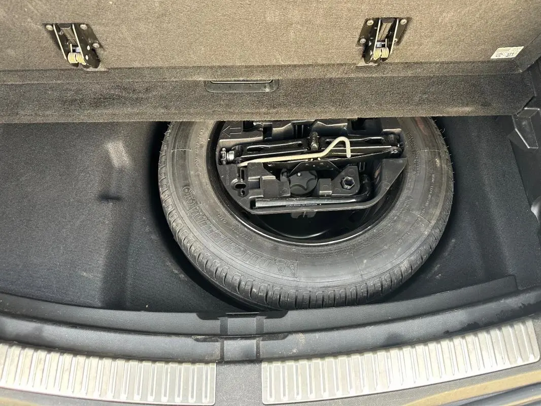 Roue de secours et outillage dans le coffre d'une Renault Mégane Break gris clair, vue plongeante sur le rangement.