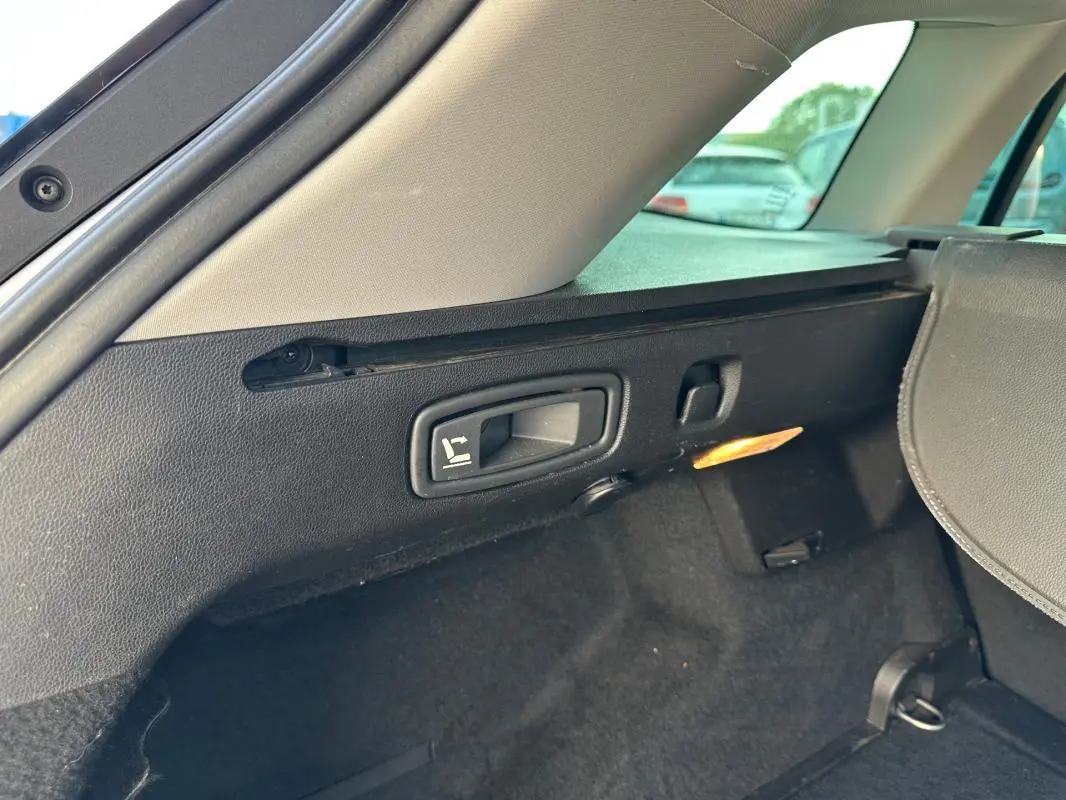 Détail de la commande de rabattement des sièges dans le coffre arrière de la Renault Mégane Break gris clair.