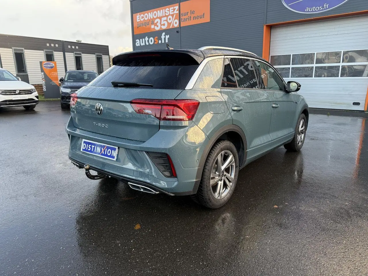 Volkswagen T-Roc bleu pétrole métallisé vu en 3/4 arrière droit avec attelage amovible sous la pluie.