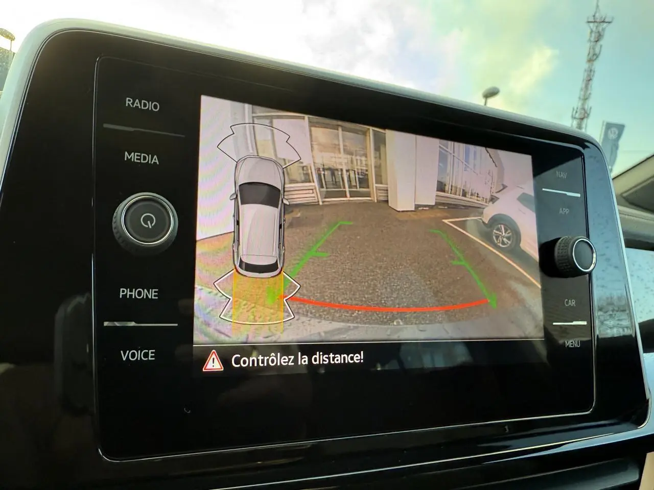 Écran de caméra de recul affichant l'arrière d'un Volkswagen T-Roc bleu pétrole en stationnement, vue intérieure console centrale.