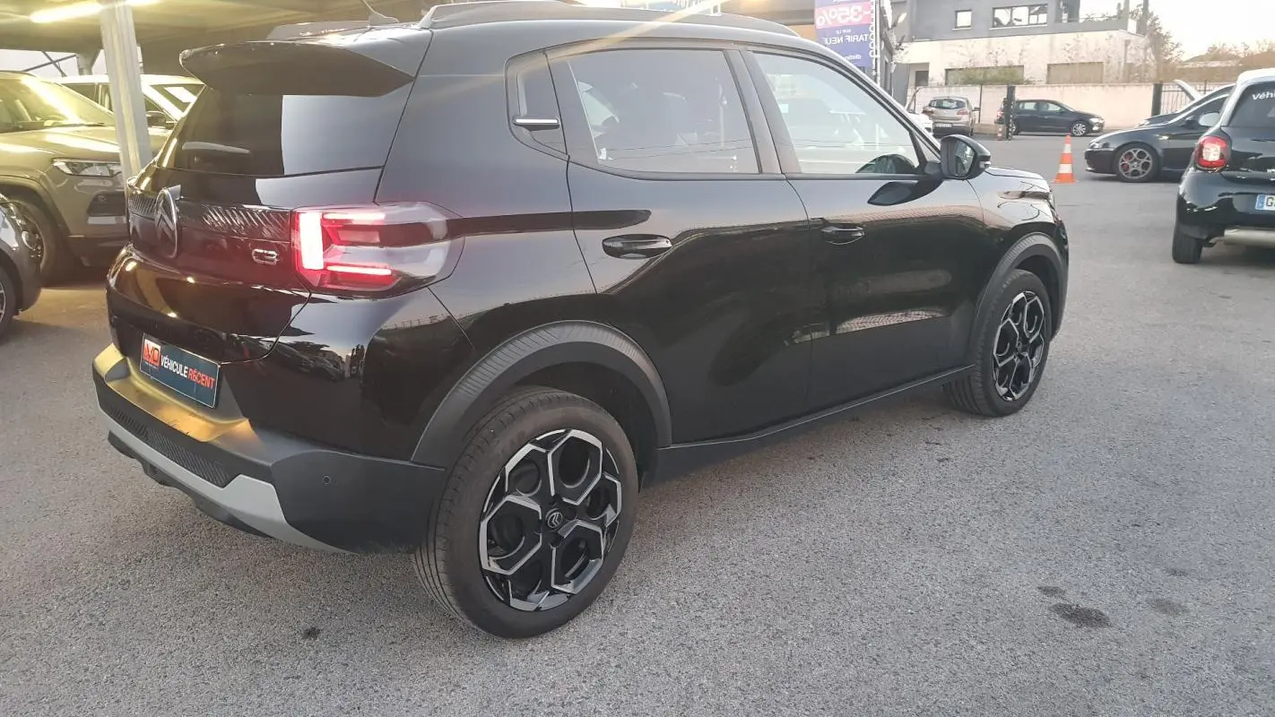 Vue 3/4 arrière droite d'une Citroën C3 noire 2025 avec jantes alliage 17 pouces et barres de toit visibles.