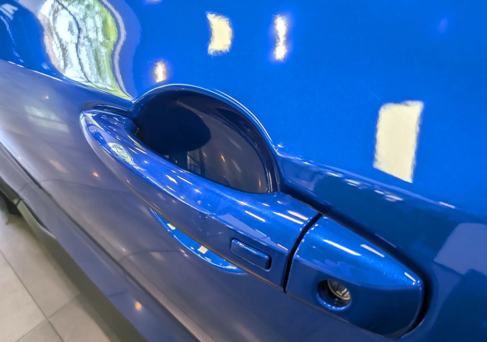 Gros plan sur la poignée de porte côté gauche du Nissan Juke Hybrid 2025 en bleu magnétique avec toit noir.