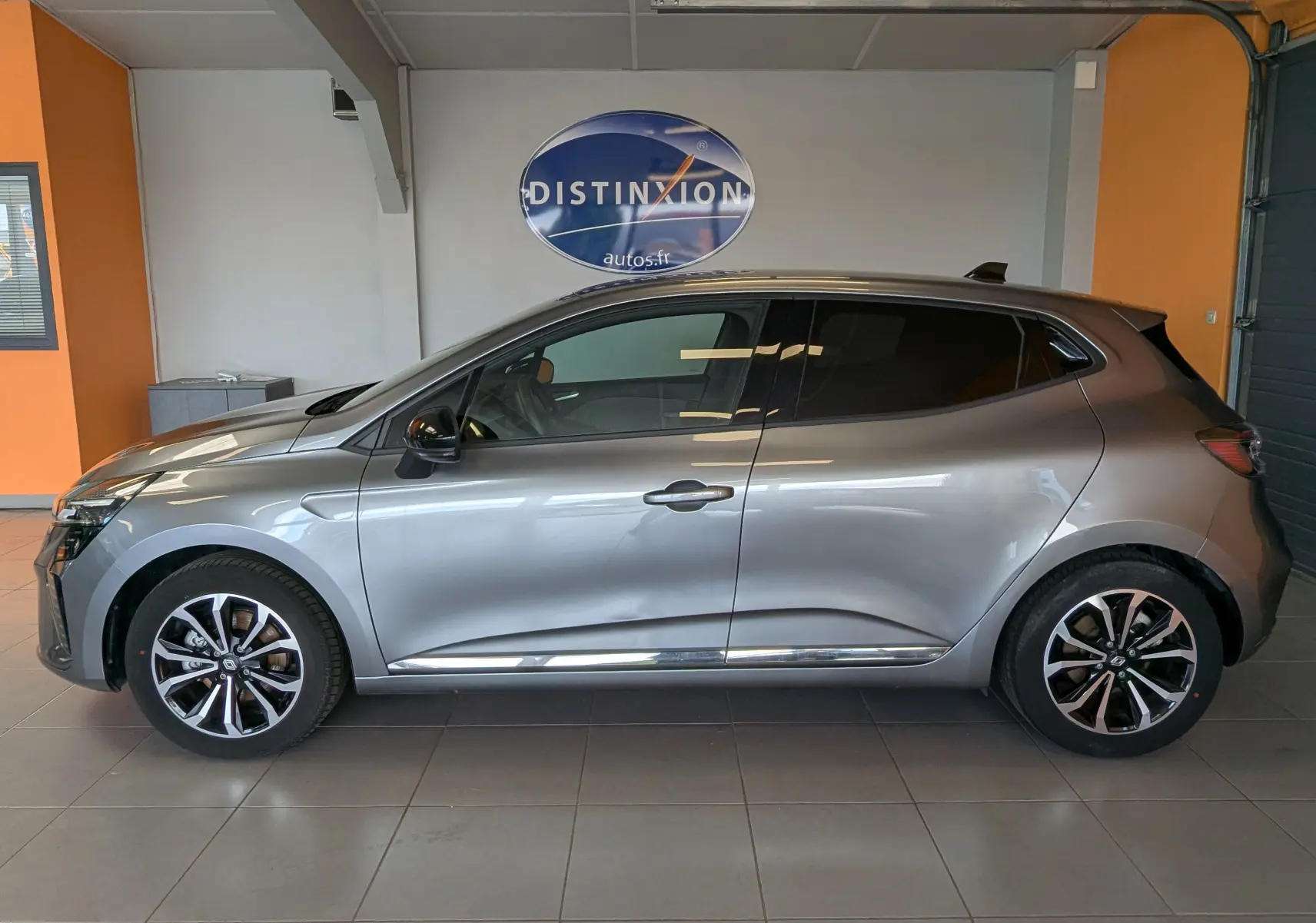 Profil côté gauche de la Renault Clio 2025 gris schiste métal, avec jantes alliage et vitres teintées en intérieur showroom.