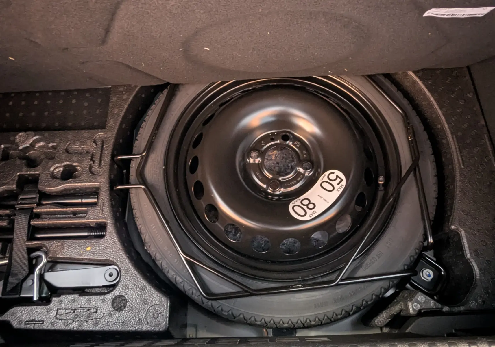 Vue en plongée sur la roue de secours et les outils de bord dans le coffre d'une Renault Clio hybride 2025.