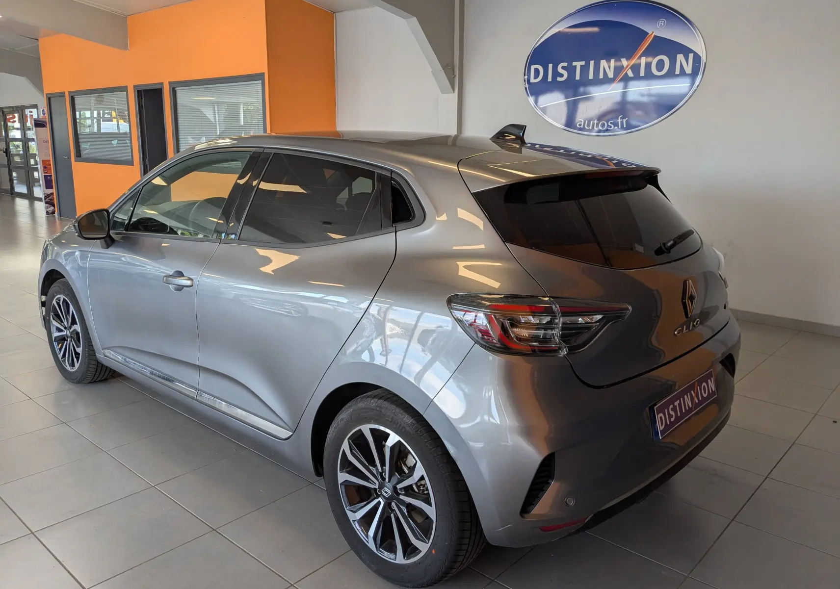 Vue 3/4 arrière droite d'une Renault Clio gris schiste métal 2025 en hybride, stationnée en intérieur avec jantes alliage distinctives.