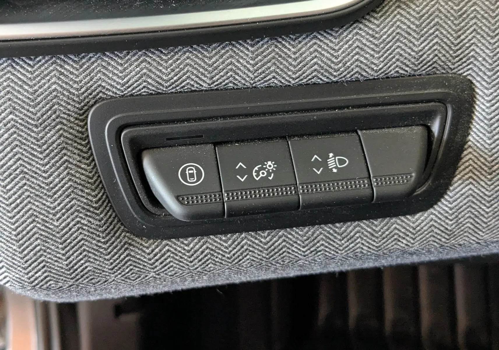 Gros plan sur les commandes d’éclairage et verrouillage intégrées dans le revêtement gris à motif chevrons de la Renault Clio hybride 2025.