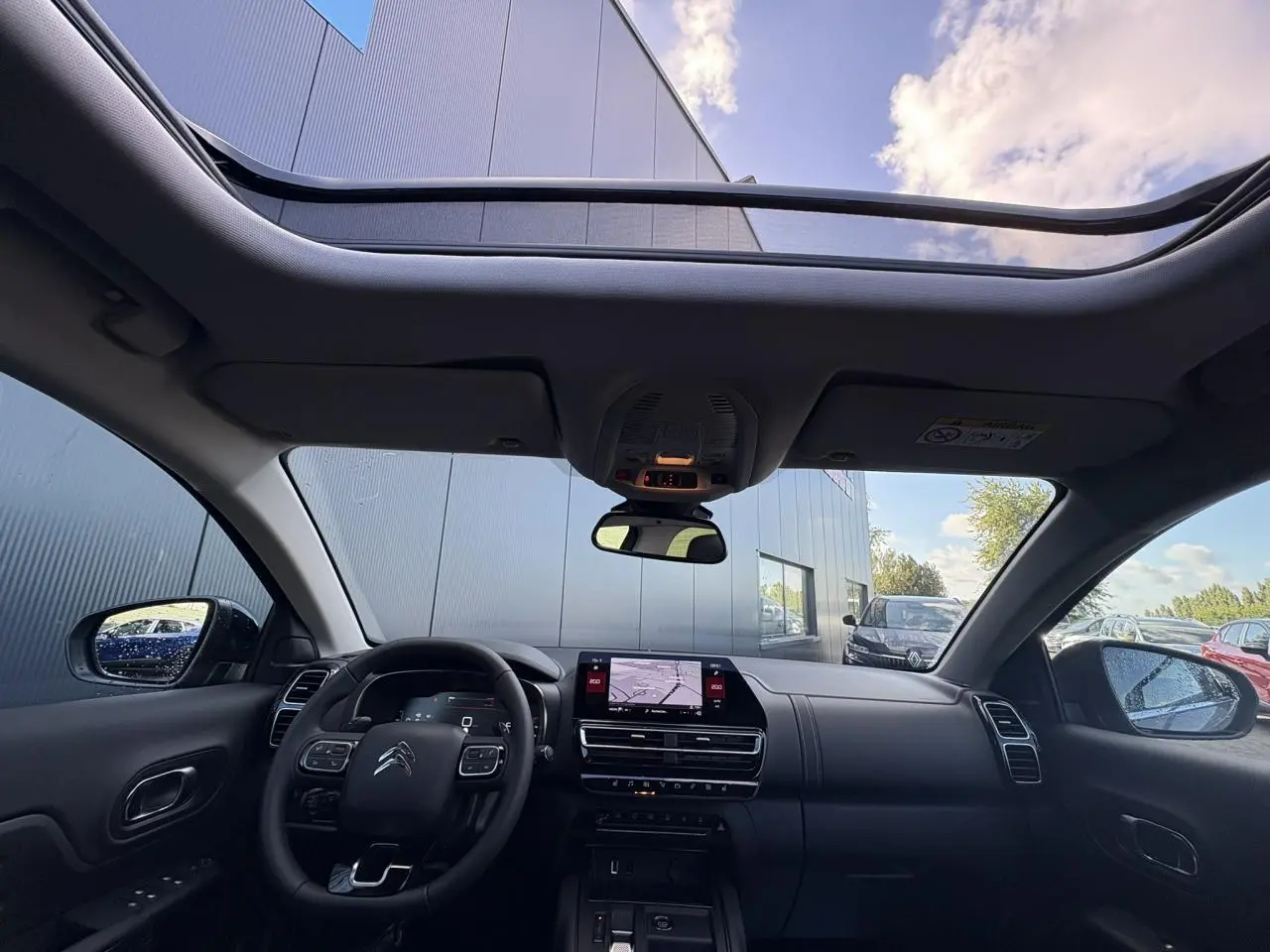 Vue intérieure avant du Citroën C5 Aircross 2025 avec toit panoramique et tableau de bord noir moderne.