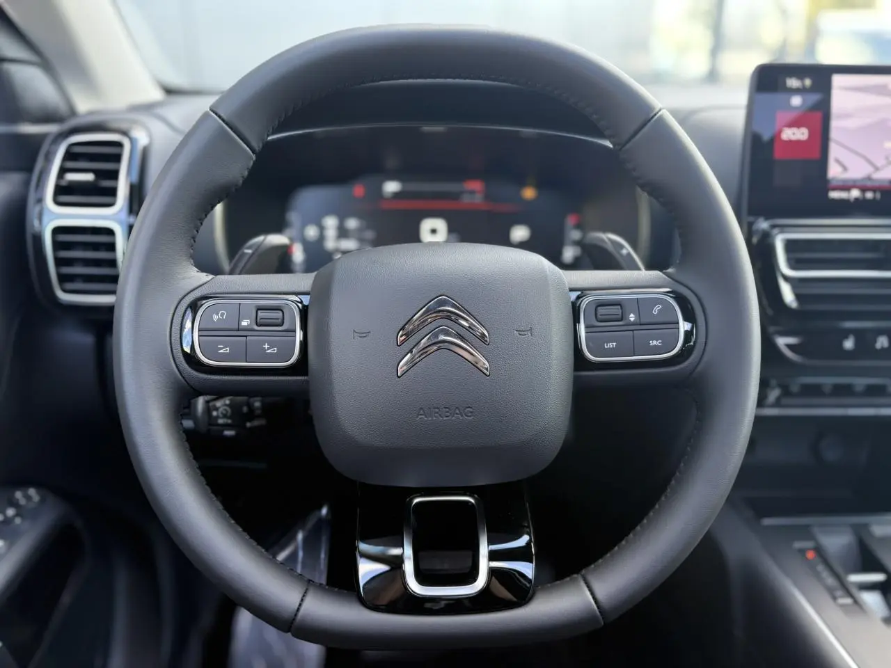 Vue rapprochée du volant cuir noir du Citroën C5 Aircross 2025 avec commandes intégrées et tableau de bord numérique flou.