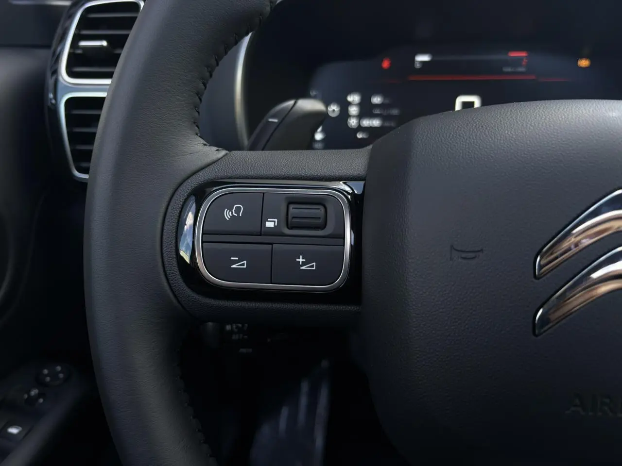 Gros plan sur les commandes gauche du volant cuir noir du Citroën C5 Aircross 2025, avec logo chrome visible.