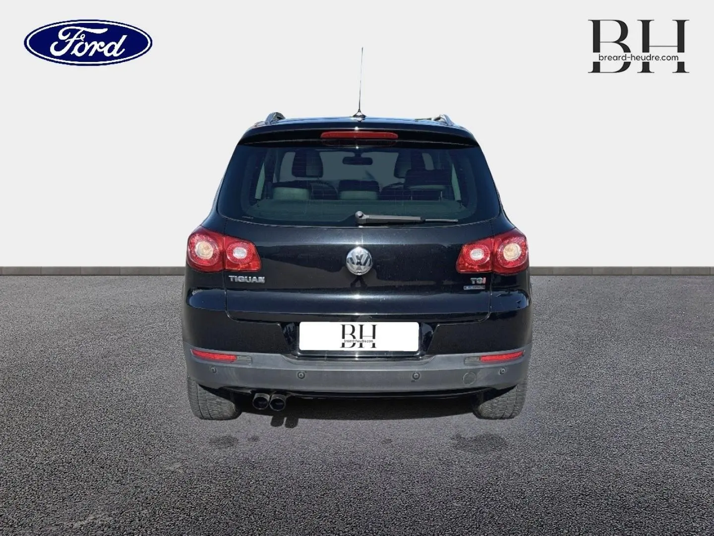 Vue arrière d'un Volkswagen Tiguan noir, avec feux arrière allumés et double sortie d'échappement visible.