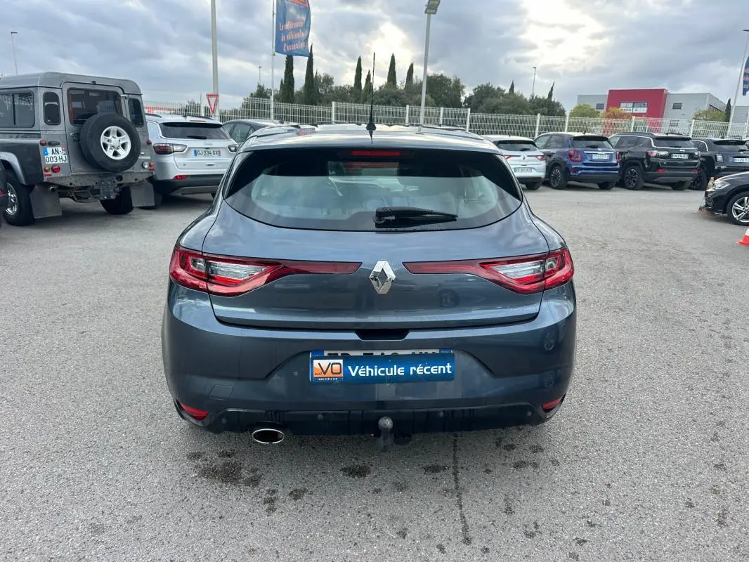 Vue arrière d'une Renault Mégane IV berline gris foncé avec feux LED et attelage de remorque visible sur parking.