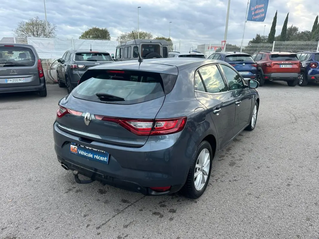Renault Mégane IV gris foncé vue 3/4 arrière droit sur parking, avec feux arrière LED et attelage visible