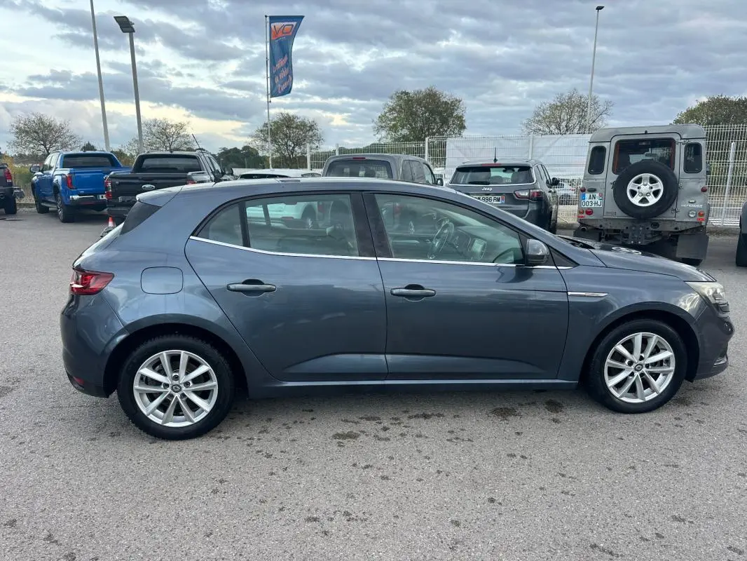 Profil côté gauche d'une Renault Mégane IV gris foncé, avec jantes alliage 18 pouces, garée en extérieur.