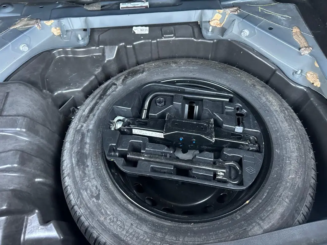 Roue de secours et kit de dépannage dans le coffre d'une Renault Mégane IV gris foncé, vue en plongée.