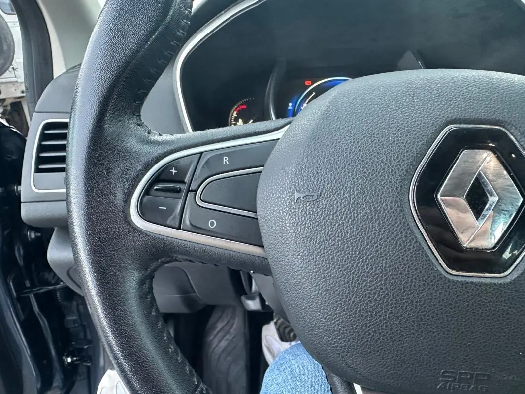 Gros plan sur le volant cuir avec commandes intégrées de la Renault Mégane IV gris foncé, tableau de bord en arrière-plan.