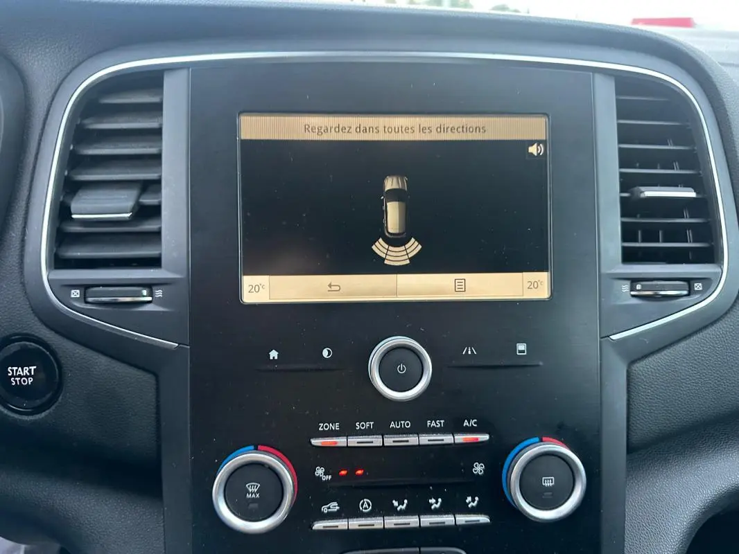 Vue rapprochée de la console centrale de la Renault Mégane IV gris foncé, affichant l'écran de détection d'obstacles et commandes climatisation.