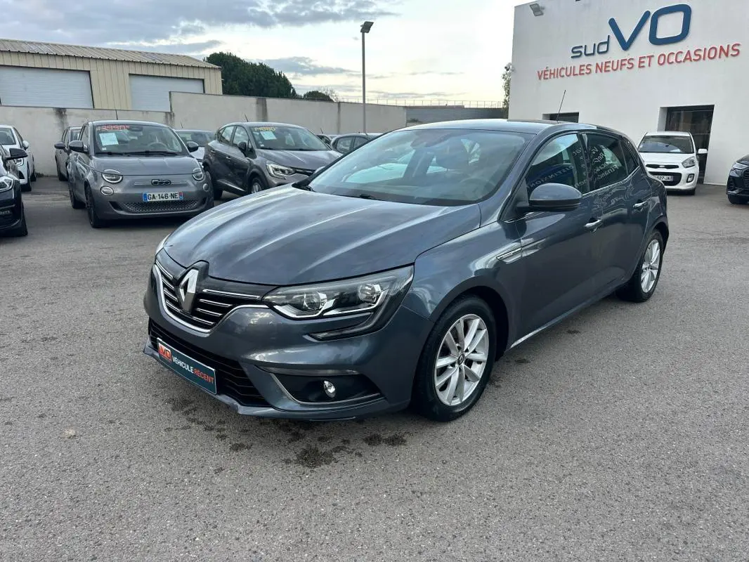 Renault Mégane IV gris foncé vue 3/4 avant droit, avec jantes alliage et phares LED allumés, sur parking extérieur.