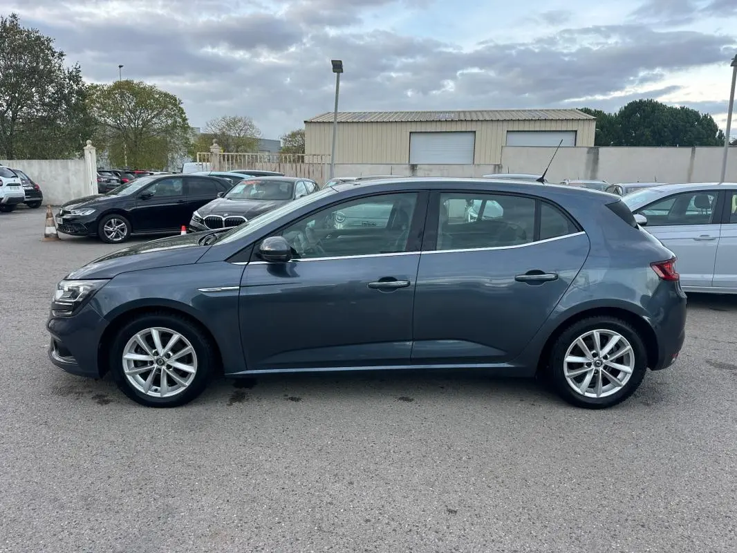 Profil côté gauche d'une Renault Mégane IV gris foncé, jantes alliage 18 pouces, garée sur un parking extérieur.