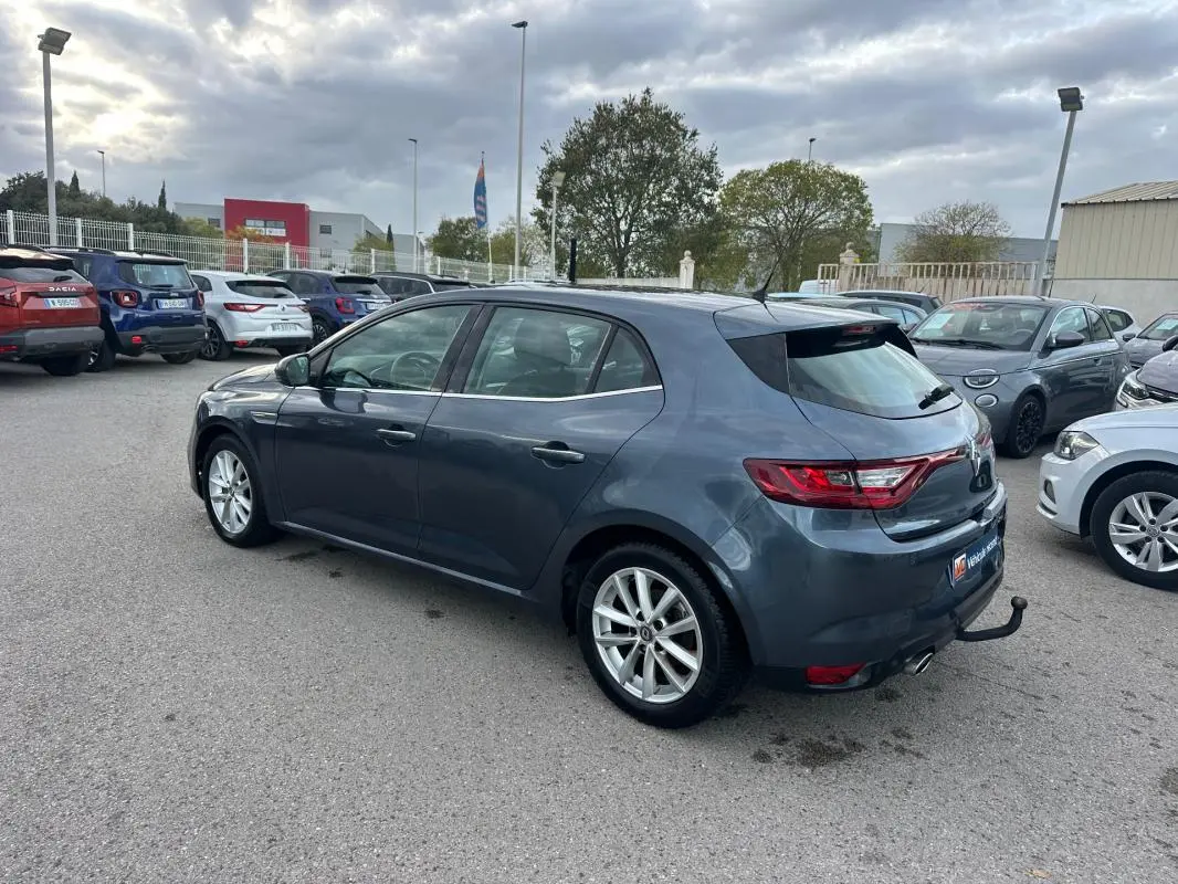 Renault Mégane IV gris foncé vue 3/4 arrière droit, jantes alliage 18 pouces et attelage visible en extérieur.